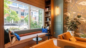 A cozy room with a large window, a bookshelf, a sofa, and a patterned wall. - 1BR | Gym, Views | Bellevue | Sophari Parkside C (Bellevue)