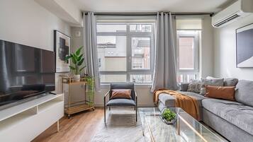 A modern living room with a flat-screen TV, a sofa, a glass coffee table, and a chair.