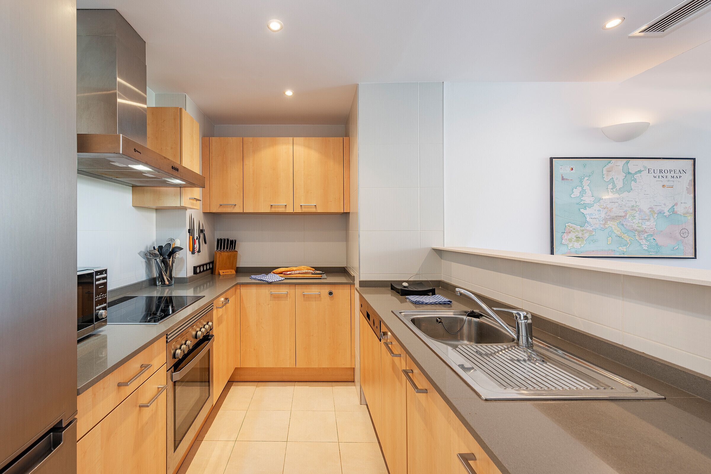 A modern kitchen with wooden cabinets, stainless steel appliances, and a European wine map on the wall.