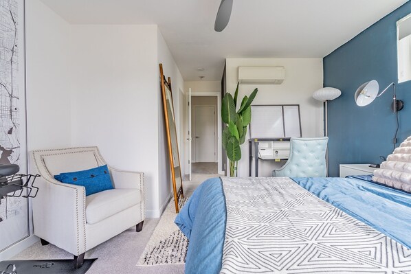 A bedroom with a bed, a chair, a desk, a plant, and a mirror. - 3BR | Rooftop | West Seattle | Sophari Home B (Seattle)