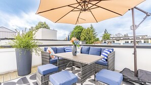 A rooftop terrace with wicker furniture, a table, and an umbrella. - 3BR | Rooftop | West Seattle | Sophari Home B (Seattle)