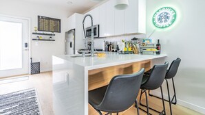 A modern kitchen with a central island, bar stools, and a neon sign. - 3BR | Rooftop | West Seattle | Sophari Home B (Seattle)