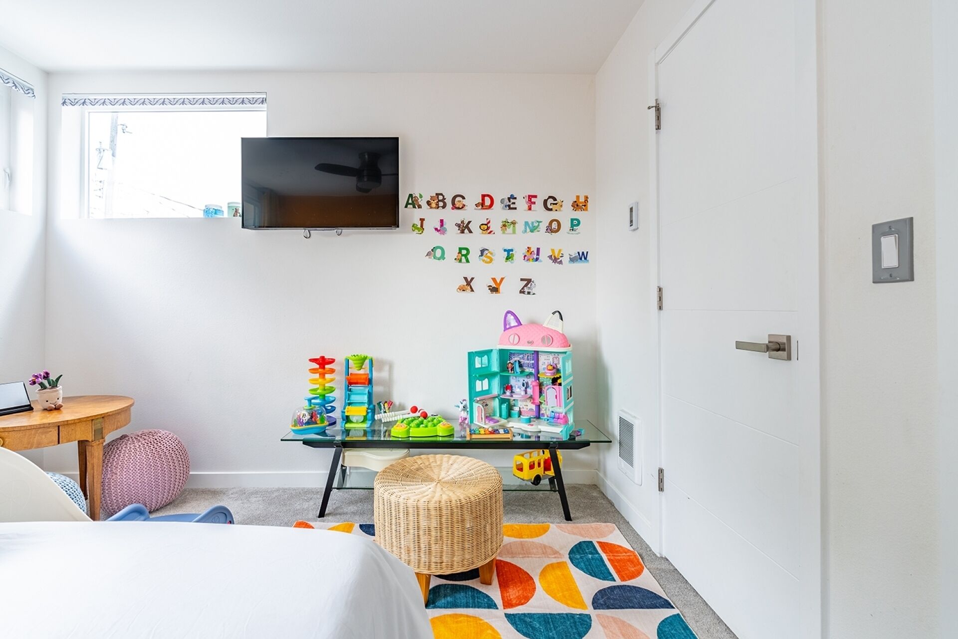 A child's play area with alphabet letters, toys, and a TV on the wall.