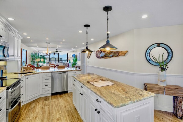 A spacious kitchen with white cabinetry, granite countertops, and pendant lighting.