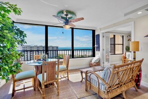 A balcony with a view of the ocean, wicker furniture, and a ceiling fan.