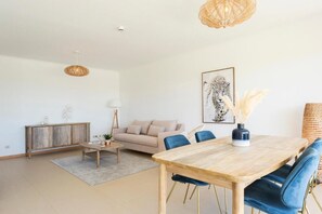 A modern living room with a wooden dining table, blue chairs, a beige sofa, and a large framed artwork on the wall. - Snazzy Varandas do Castelo By Garvetur One Bedroom Apartment Sleeps 2 Persons (Albufeira)