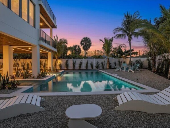 A modern pool area with a clear pool, lounge chairs, and a building with a balcony.