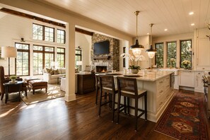 A spacious kitchen with a large island, wooden flooring, and a stone fireplace. - Boathouse: Lakefront Highlands Retreat | Canoe + Gated (Highlands)