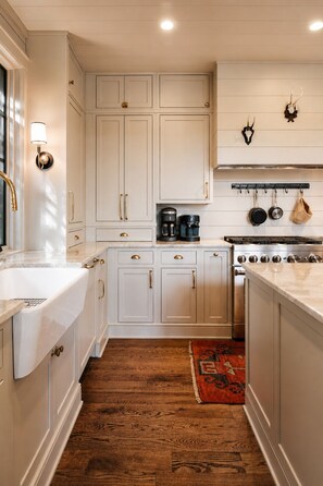 A kitchen with white cabinetry, a stainless steel stove, and a coffee maker. - Boathouse: Lakefront Highlands Retreat | Canoe + Gated (Highlands)
