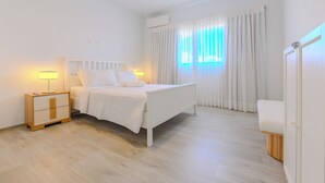 A bedroom with a bed, bedside tables, a nightstand, a window with curtains, and a door. - Tracadero Lodge Con Acceso al Beach Club (Dominicus)