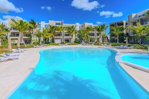 A resort pool area with multiple lounge chairs and palm trees, surrounded by modern buildings. - Tracadero Lodge Con Acceso al Beach Club (Dominicus)