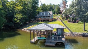 Un chalet au bord du lac, doté d’un quai, d’un espace salon abrité et d’une grande maison en arrière-plan.