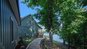 Une maison avec un chemin de pierre menant à un quai au bord d’un lac, entourée d’arbres.