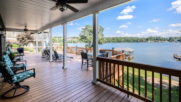 Une terrasse couverte avec un plancher en bois, du mobilier d’extérieur et une vue sur un lac.