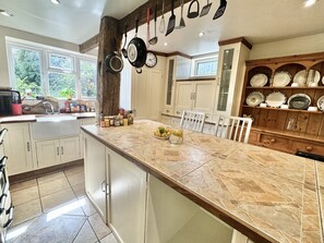 A kitchen with a large island, white cabinets, and a variety of kitchen utensils hanging above. - Forest Cottage (Southampton)