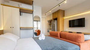 A modern hotel room with a bed, a sofa, a TV, and a kitchenette. - Studios in Building With Gym in Brooklin - SP Emnrs (São Paulo)