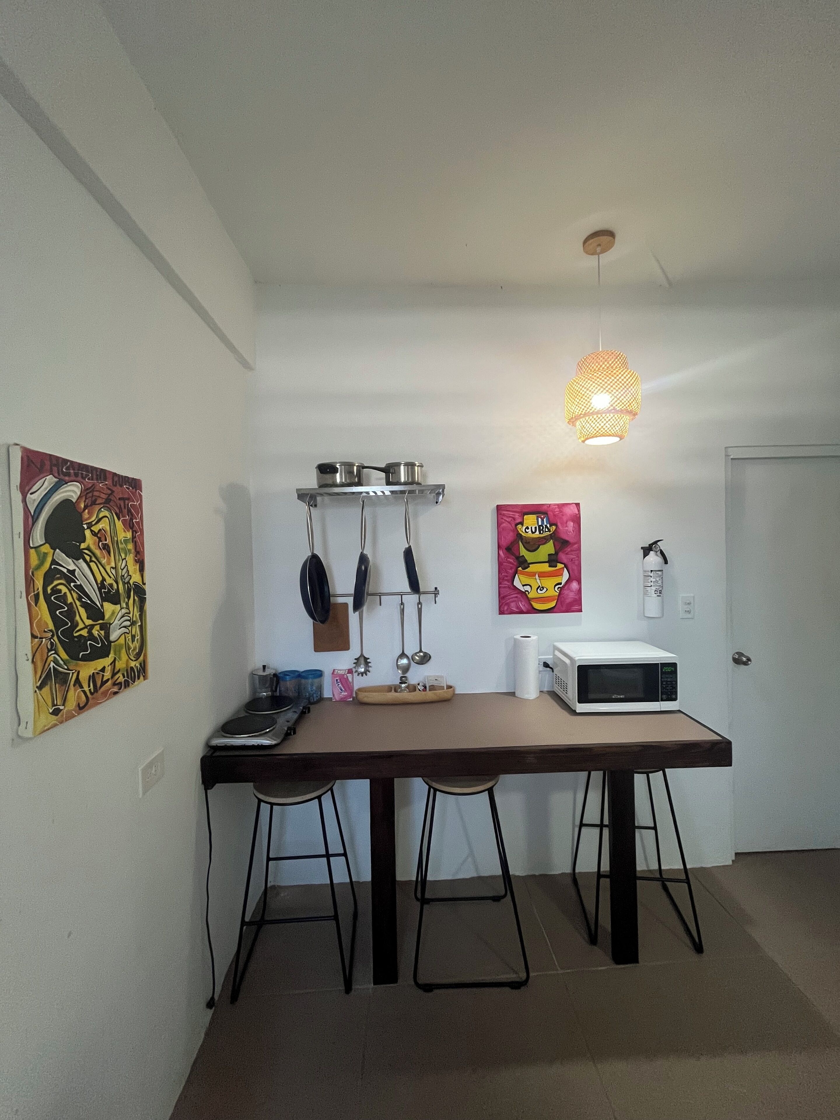 A kitchen with a microwave, hanging pots, and a hanging light fixture.