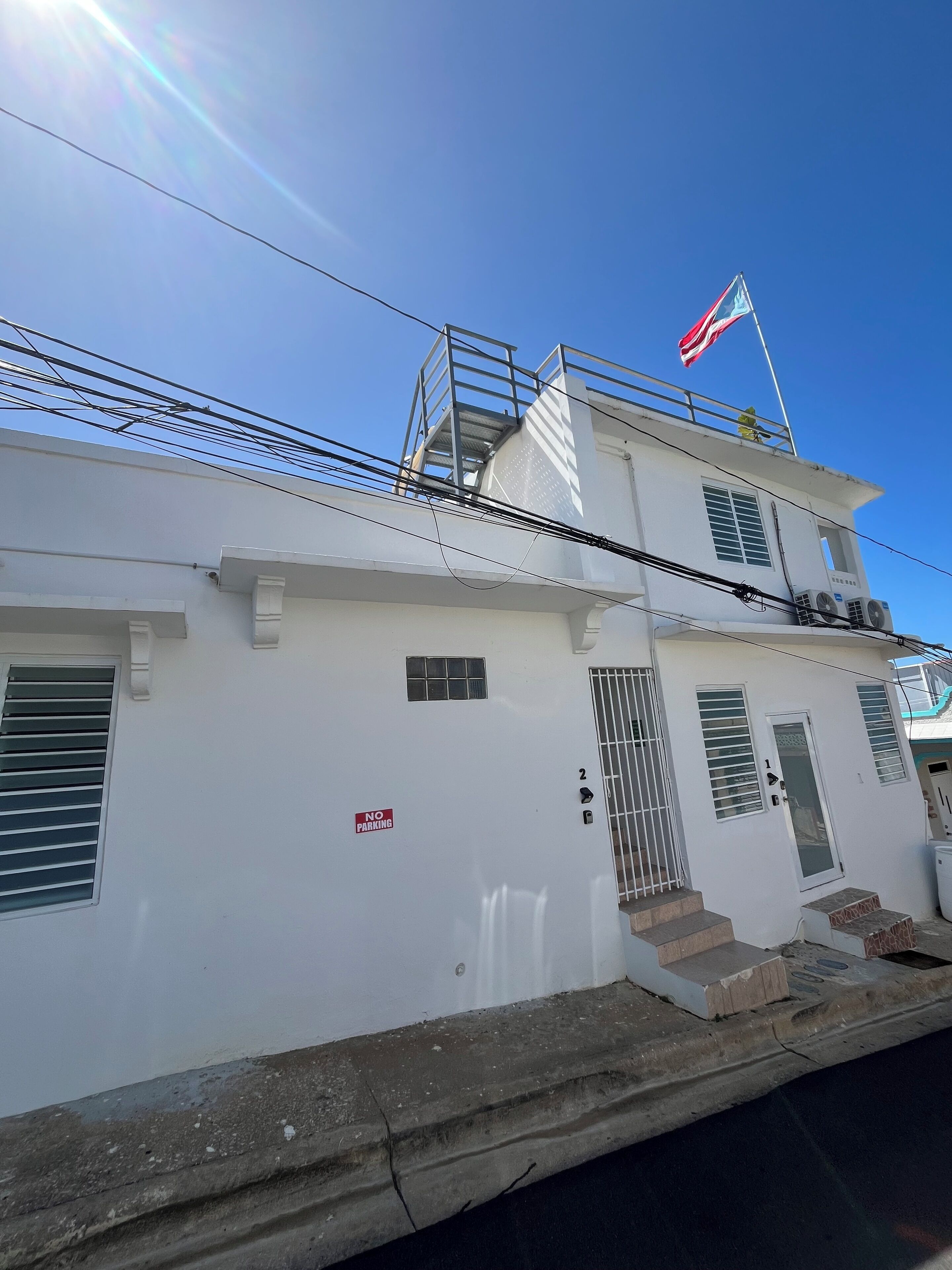 A white building with a "NO PARKING" sign, a staircase, and a flagpole with a flag.