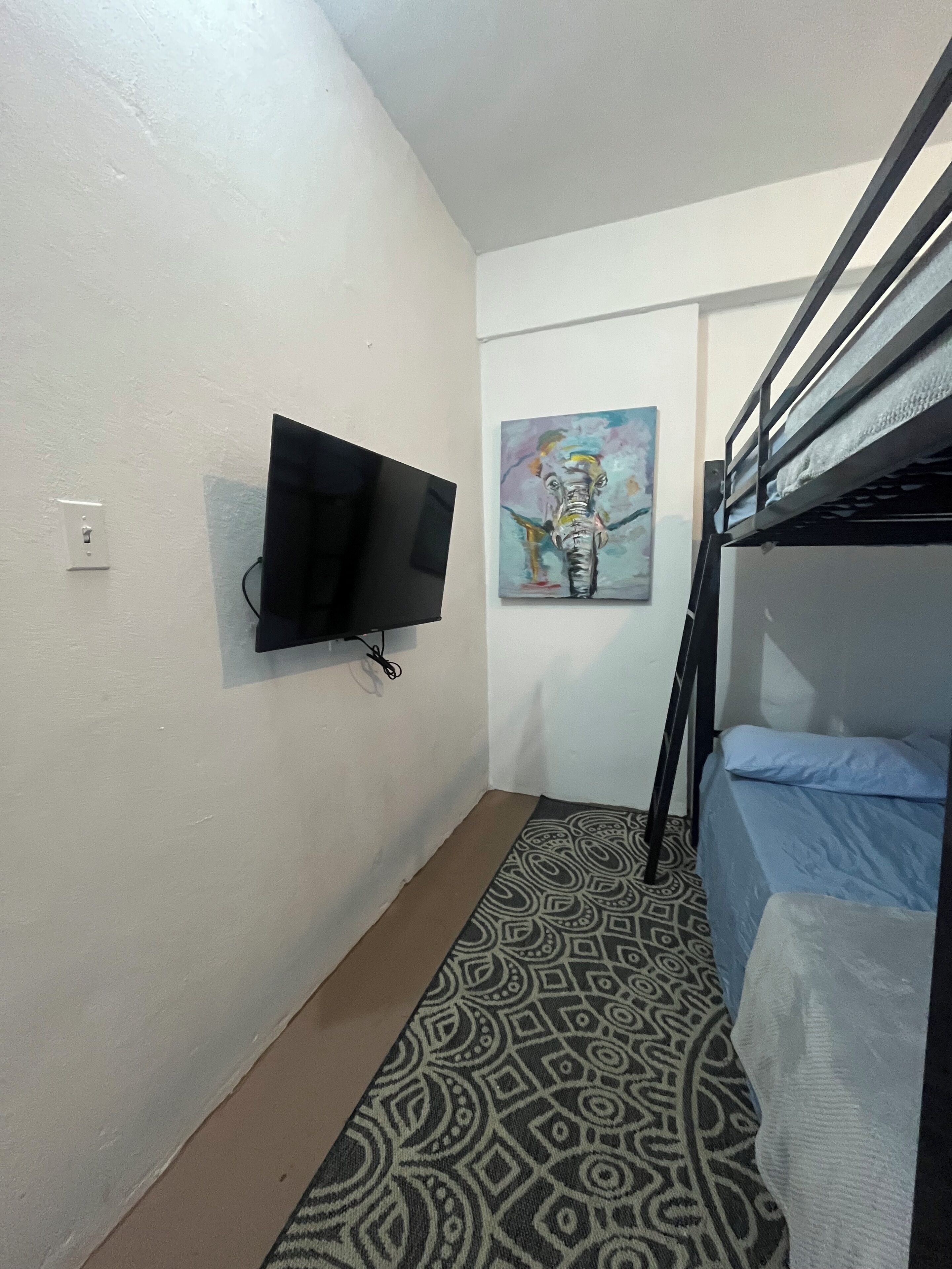 Ein kleiner, schmaler Raum mit einem Etagenbett, einem an der Wand montierten Flachbildfernseher und einem Teppich mit Muster.