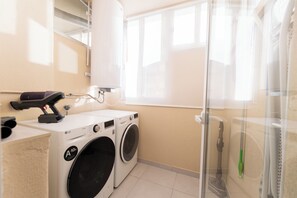 Un espace buanderie équipé de deux machines à laver, d’un sèche-linge et d’une cabine de douche en verre.