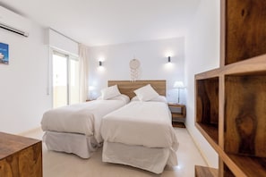 Een slaapkamer met twee bedden, een houten hoofdbord, nachtlampjes en een droomvanger aan de muur.