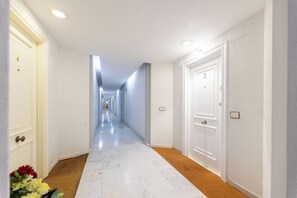 Un long couloir étroit aux murs blancs, avec des portes de part et d’autre.