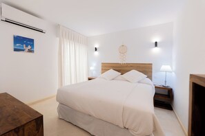 Une chambre à coucher bien rangée, avec un grand lit, des tables de chevet, un climatiseur fixé au mur, un attrape-rêves et un tableau encadré accroché au mur.