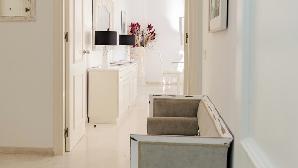 A hallway with a white dresser, a mirror, a vase with flowers, and a chair. - Your Dream Vacation (Marbella)