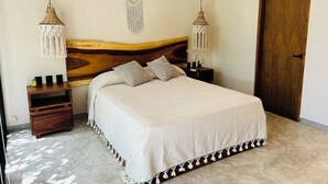 Ein Schlafzimmer mit einem Bett, zwei Nachttischen, einem Holzkopfende und zwei Wandbehängen aus Makramee.