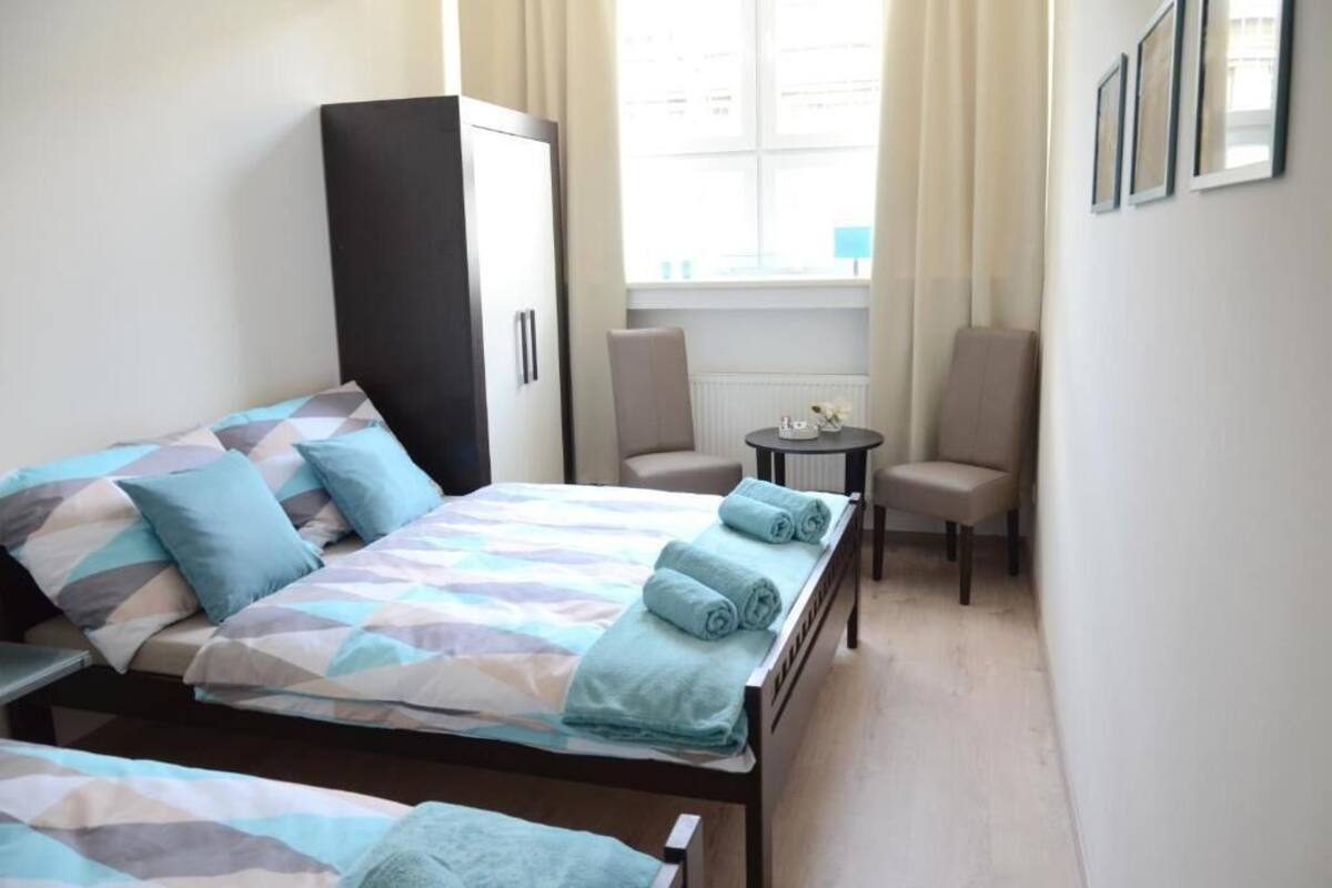 A hotel room with two beds, a wardrobe, a small table, and a chair.