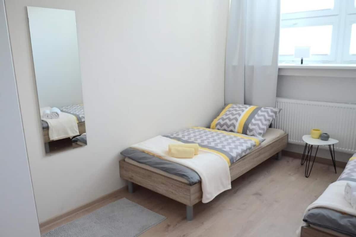 A bedroom with a bed, a small table, a mirror, and a window.