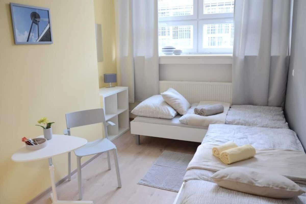 A bedroom with a bed, a chair, a small table, and a window with curtains.