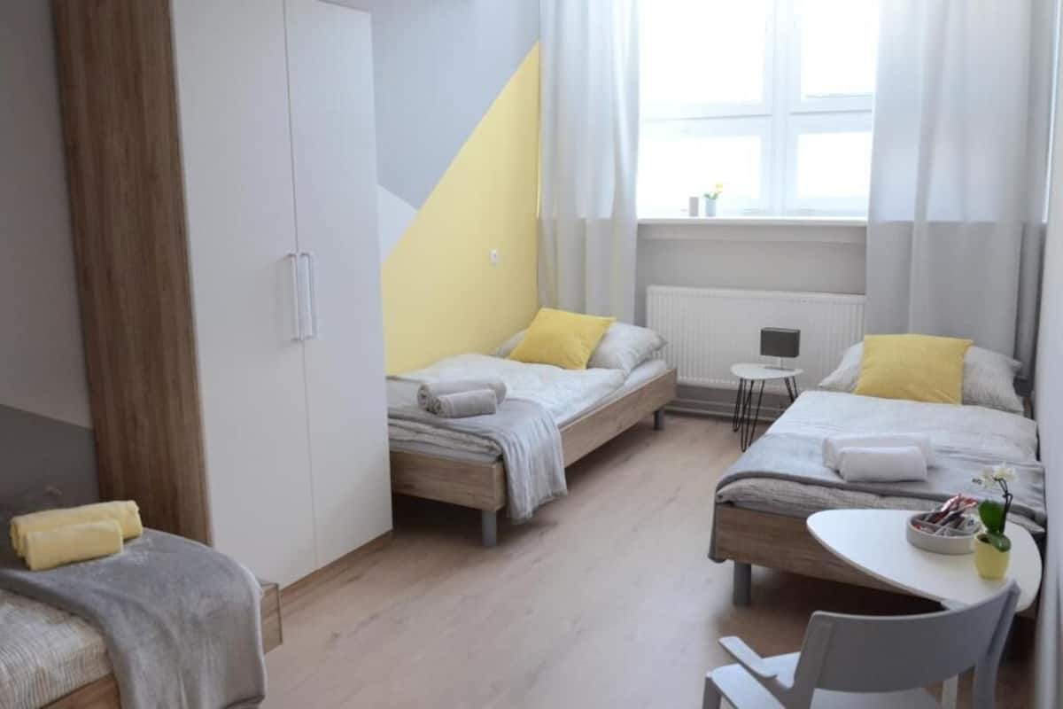 A modern bedroom with two beds, a small table, and a chair.