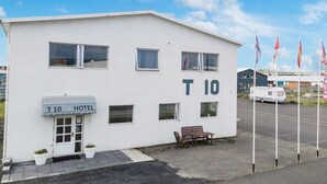 A white building with a sign reading "T 10 HOTEL" and a number "10" on the side. There are flags in front of the building. - T10 Self check-in Hotel (Hafnarfjörður)