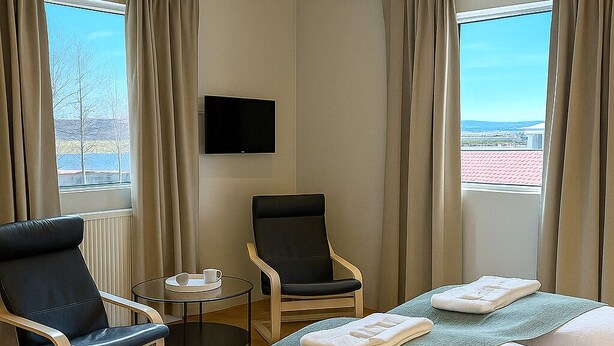 A hotel room with a bed, two chairs, a small table, a TV, and a view of the outdoors. - T10 Self check-in Hotel (Hafnarfjörður)