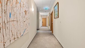 A hallway with a large abstract painting on the left, a wooden door at the end, and a framed picture on the right wall. - T10 Self check-in Hotel (Hafnarfjörður)
