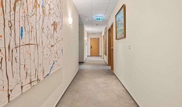Käytävän vasemmalla puolella on suuri abstrakti maalaus, käytävän päässä puinen ovi ja oikean seinän puolella kehystetty kuva.