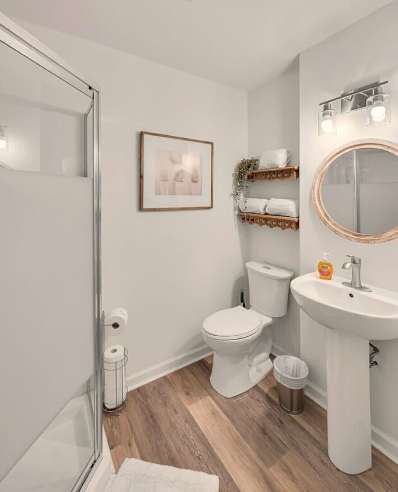 A modern bathroom with a toilet, sink, and shower. There is a framed picture on the wall and a shelf with towels.