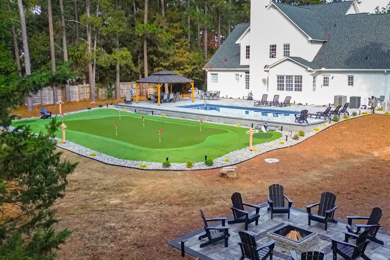 Una casa grande con piscina, un patio con mobiliario exterior y un césped cuidado.