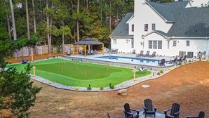 A large house with a swimming pool, a patio with outdoor furniture, and a well-maintained lawn. - Luxury Golf Retreat - Simulator & Short Game Setup (Southern Pines)
