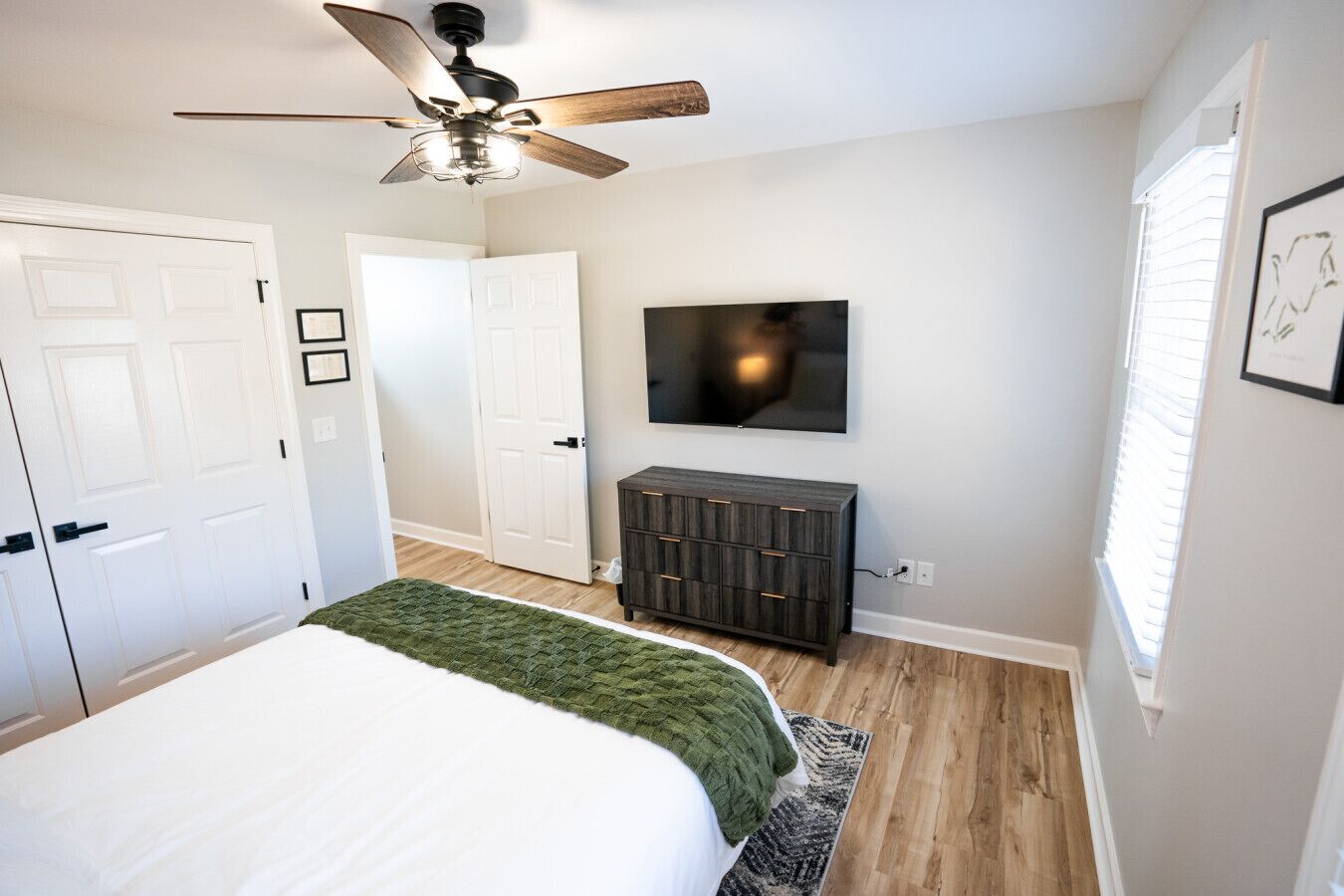 Ein Schlafzimmer mit Bett, Deckenventilator, Wandfernseher und Kommode.