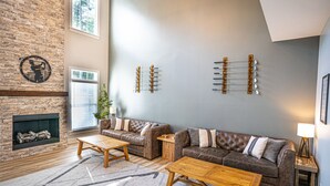 A living room with a brick fireplace, two sofas, a coffee table, and a wall-mounted guitar. - Luxury Golf Retreat - Simulator & Short Game Setup (Southern Pines)