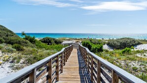 Een houten vlonder die naar een strand leidt, met heldere lucht en uitzicht op de oceaan.