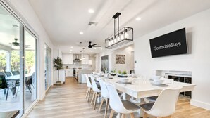 A modern kitchen with a dining area, a TV mounted on the wall, and a view of the outdoors. - Scottsdalestays Multimillion Estate on Huge Acre Lot-Pool-Slide-Sports Courts (Scottsdale)