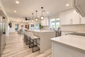 A modern kitchen with a central island, bar stools, pendant lighting, and a ceiling fan.