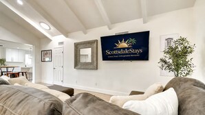 A living room with a large flat-screen TV, a sofa, and a potted plant. - Scottsdalestays Multimillion Estate on Huge Acre Lot-Pool-Slide-Sports Courts (Scottsdale)