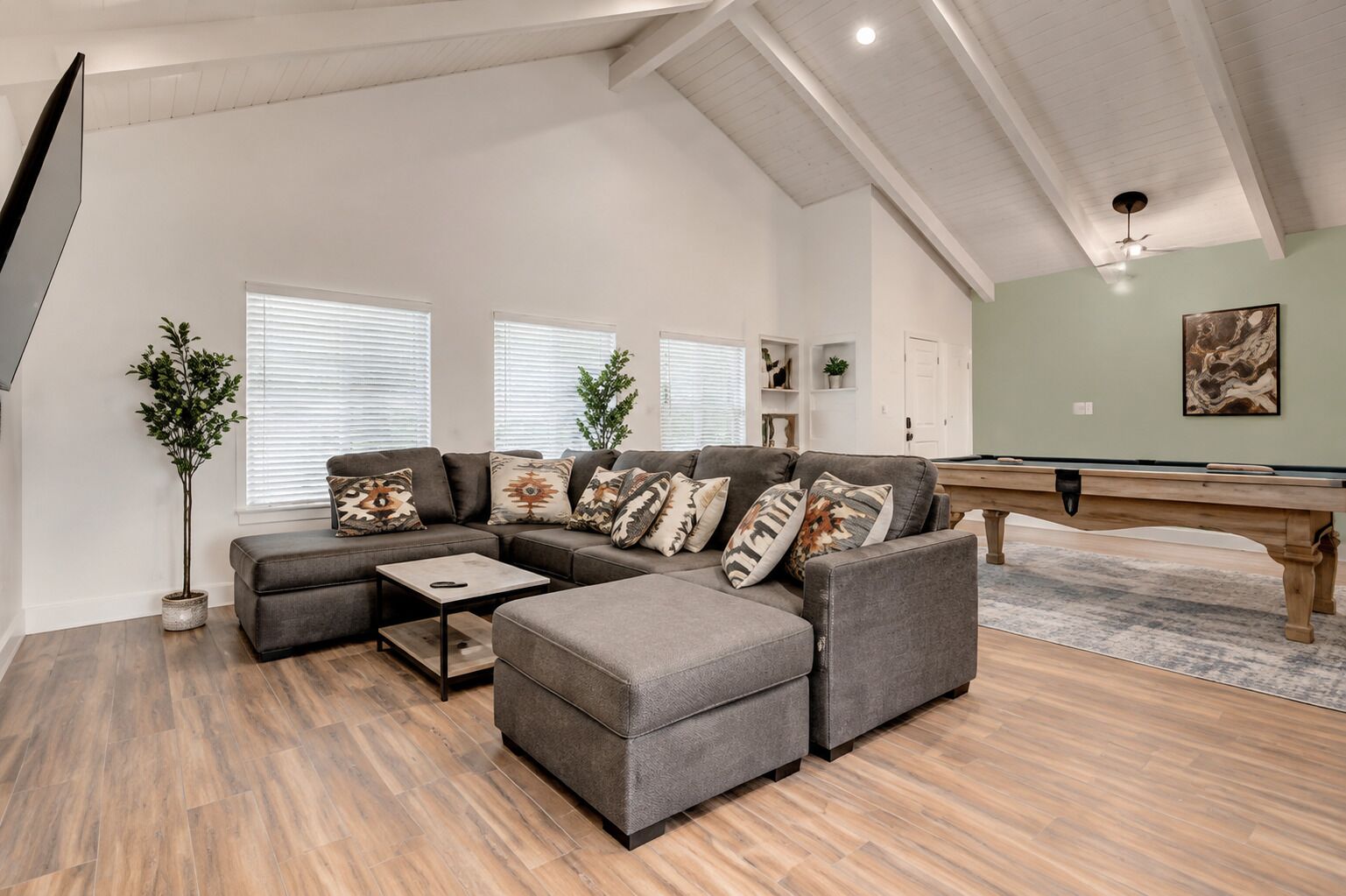A modern living room with a sectional sofa, a pool table, and a ceiling fan.