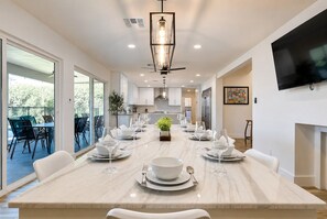 A modern dining area with a marble table set for a meal, a ceiling fan, and a flat-screen TV mounted on the wall.