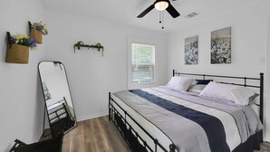 Un dormitorio con cama, ventilador de techo, ventana con persianas y adornos en la pared.