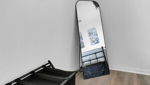 Una habitación con un banco de metal negro, un espejo grande y dos cestas tejidas con flores en la pared.